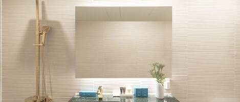 A bathroom with a large mirror, a shower with a gold fixture, a sink with a marble countertop, and a toilet.