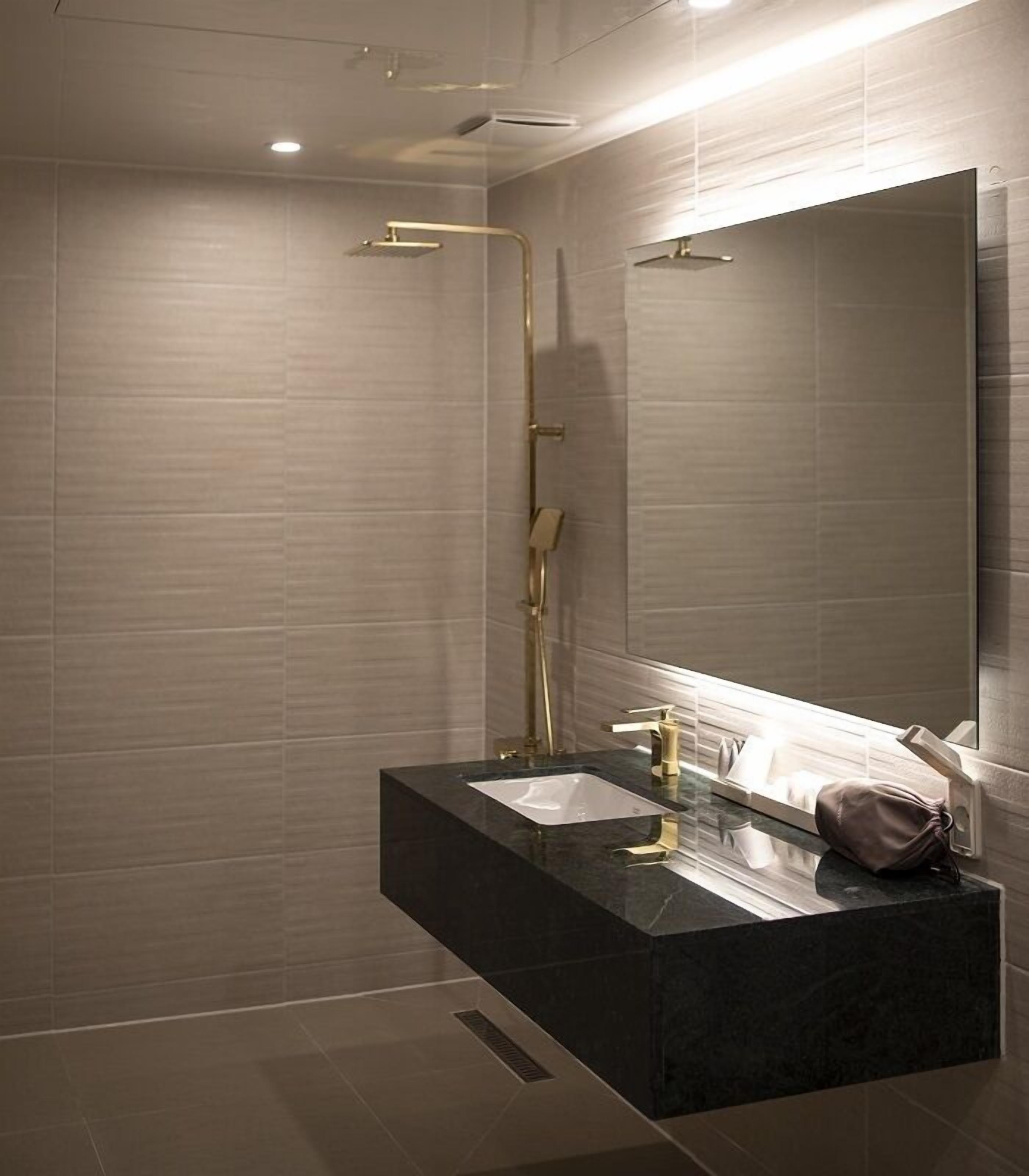 Un baño moderno con tocador negro, un espejo grande y una ducha con detalles dorados.