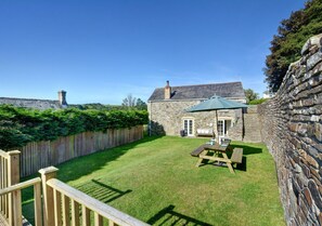Relax in a serene backyard with a traditional stone building, lawn, and wooden deck, perfect for outdoor activities and casual dining.