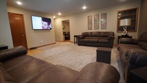 A living room with a brown leather sofa, a TV mounted on the wall, and a lamp on a side table. - Five Bedrooms and a Great Location (Sioux Falls)
