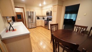 A modern kitchen with wooden cabinets, stainless steel appliances, and a dining area with wooden chairs. - Five Bedrooms and a Great Location (Sioux Falls)