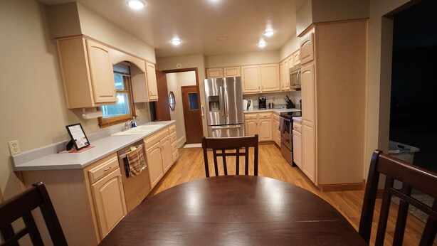 A kitchen with wooden cabinets, a stainless steel refrigerator, and a dining table with chairs. - Five Bedrooms and a Great Location (Sioux Falls)