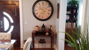 Un coin repas avec une table et des chaises en bois, un tapis vert et une horloge murale.