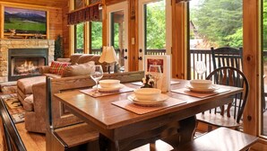 A cozy cabin interior with a fireplace, wooden furniture, and large windows offering a view of the outdoors. - Best Location/HotTub/Resort Pool/Game Rm/Fast WiFi
Dollywood 2 minutes away! (Sevierville)