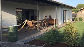 A covered outdoor seating area with wooden chairs and a table, a trash can, and a small garden with plants and flowers. - Pleasant house on the Arcachon basin (La Teste-de-Buch)