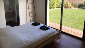 A bedroom with a large window, a wooden bed frame, and a view of a grassy yard. - Pleasant house on the Arcachon basin (La Teste-de-Buch)