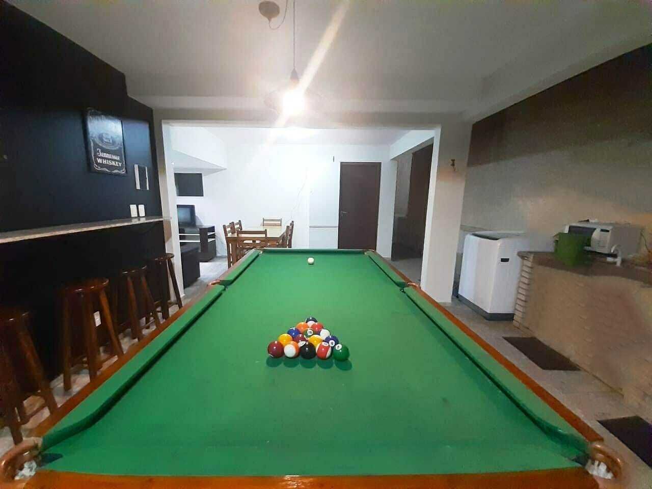 A pool table with balls arranged in a triangle, a refrigerator, and a bar area with stools.