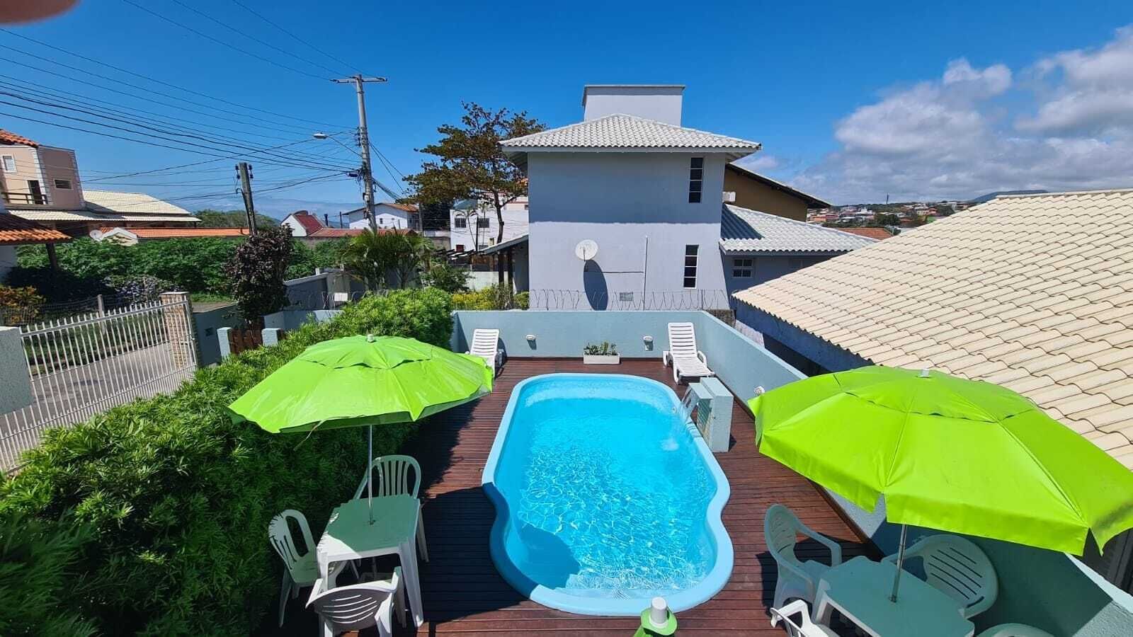 Une piscine sur le toit, agrémentée de deux parasols verts, entourée d’une terrasse en bois et de chaises blanches.
