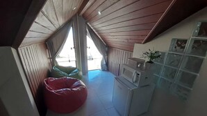 Eine kleine, kompakte Küche mit Mikrowelle, Spüle und Schränken. Ein rotes Sitzsack und ein Fenster sorgen für natürliches Licht.