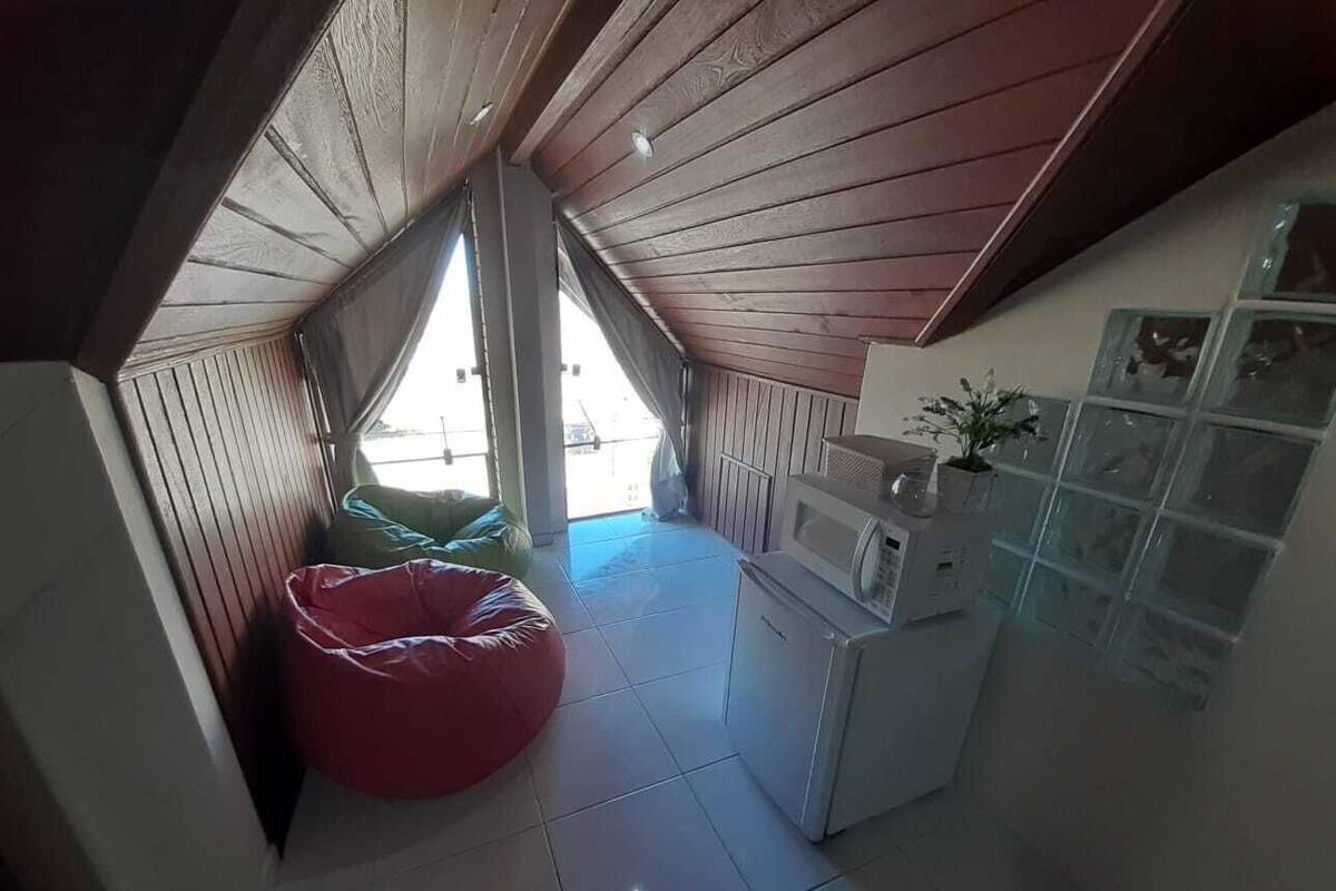 Cocina pequeña y funcional con microondas, lavamanos y armarios. Hay un sillón de peluche rojo y una ventana que proporciona luz natural.