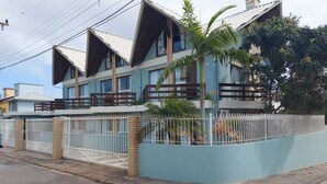 Ein zweistöckiges Haus mit blauer Fassade, weißem Zaun und einem Palmenbaum davor.
