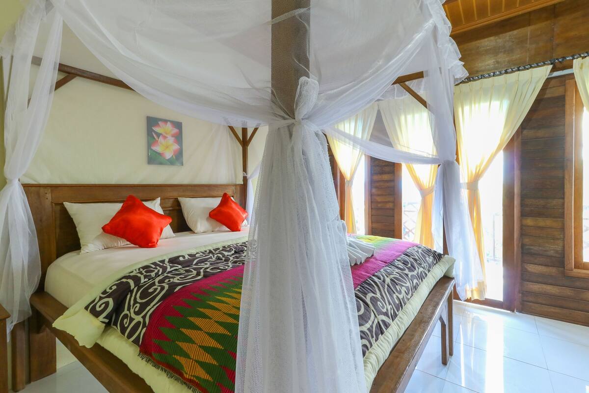 A bed with a canopy, pillows, and a colorful blanket.