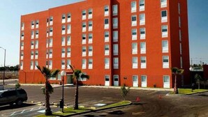 A multi-story red building with a uniform facade, rectangular windows, and a parking lot with palm trees. - Hotel Tecnologico Norte (Chihuahua)