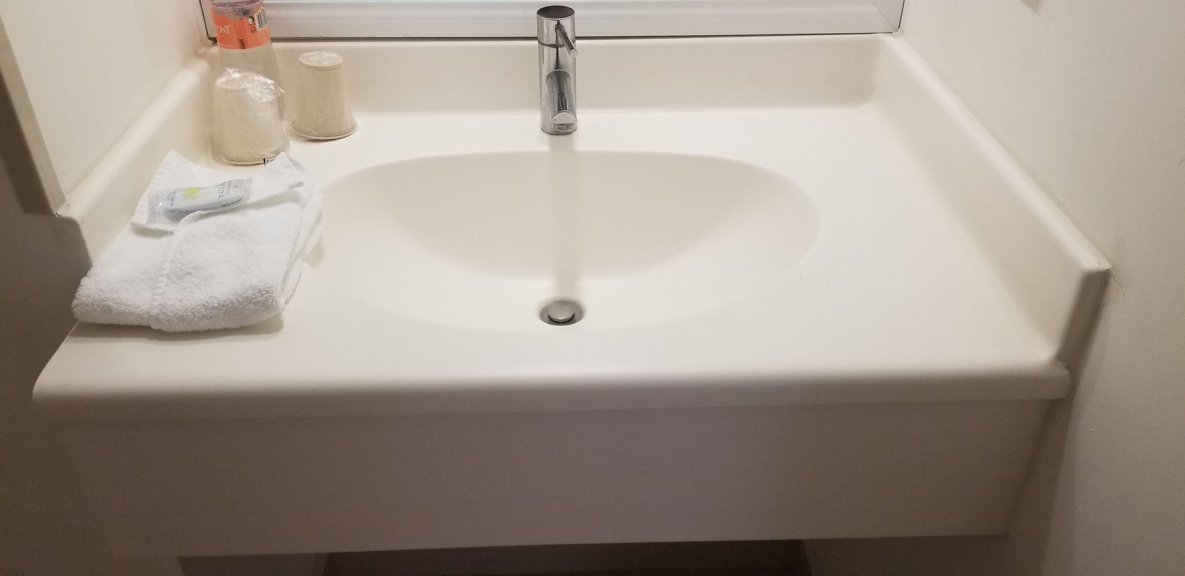 A white bathroom sink with a chrome faucet, a white towel, and a bottle of liquid soap.