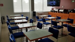A classroom with tables and chairs, a projector screen, and a coffee machine. - Hotel Tecnologico Norte (Chihuahua)