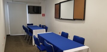 Una sala de conferencias con mesas y sillas azules, una pizarra y un televisor en la pared.