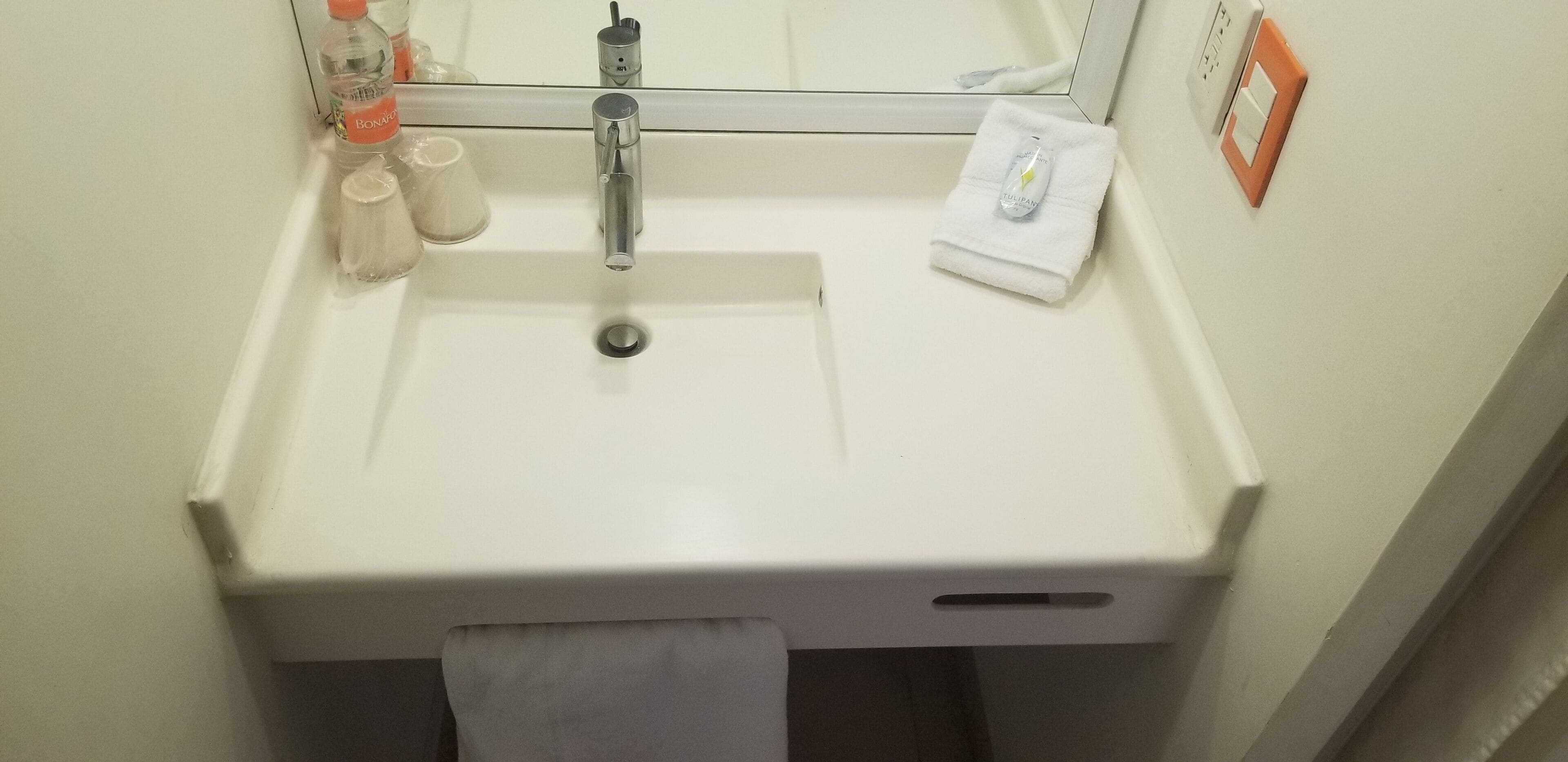 Un lavabo blanco con espejo, una toalla colgada en la pared y artículos de aseo sobre la encimera.