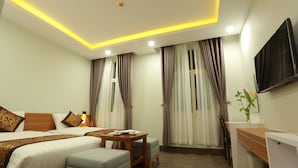 Quarto de hotel com uma cama, uma escrivaninha, uma cadeira, uma televisão e cortinas.