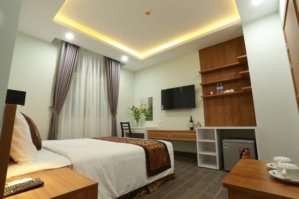 Una habitación de hotel con cama, mesita de noche, televisión, escritorio y una pequeña kitchenette.