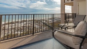 A balcony with a view of the beach, a chair, and a small pool.