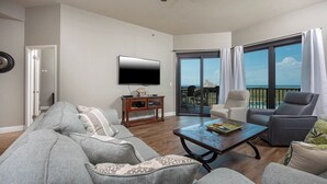 A living room with a grey sofa, a coffee table, a TV, and a balcony with a view.
