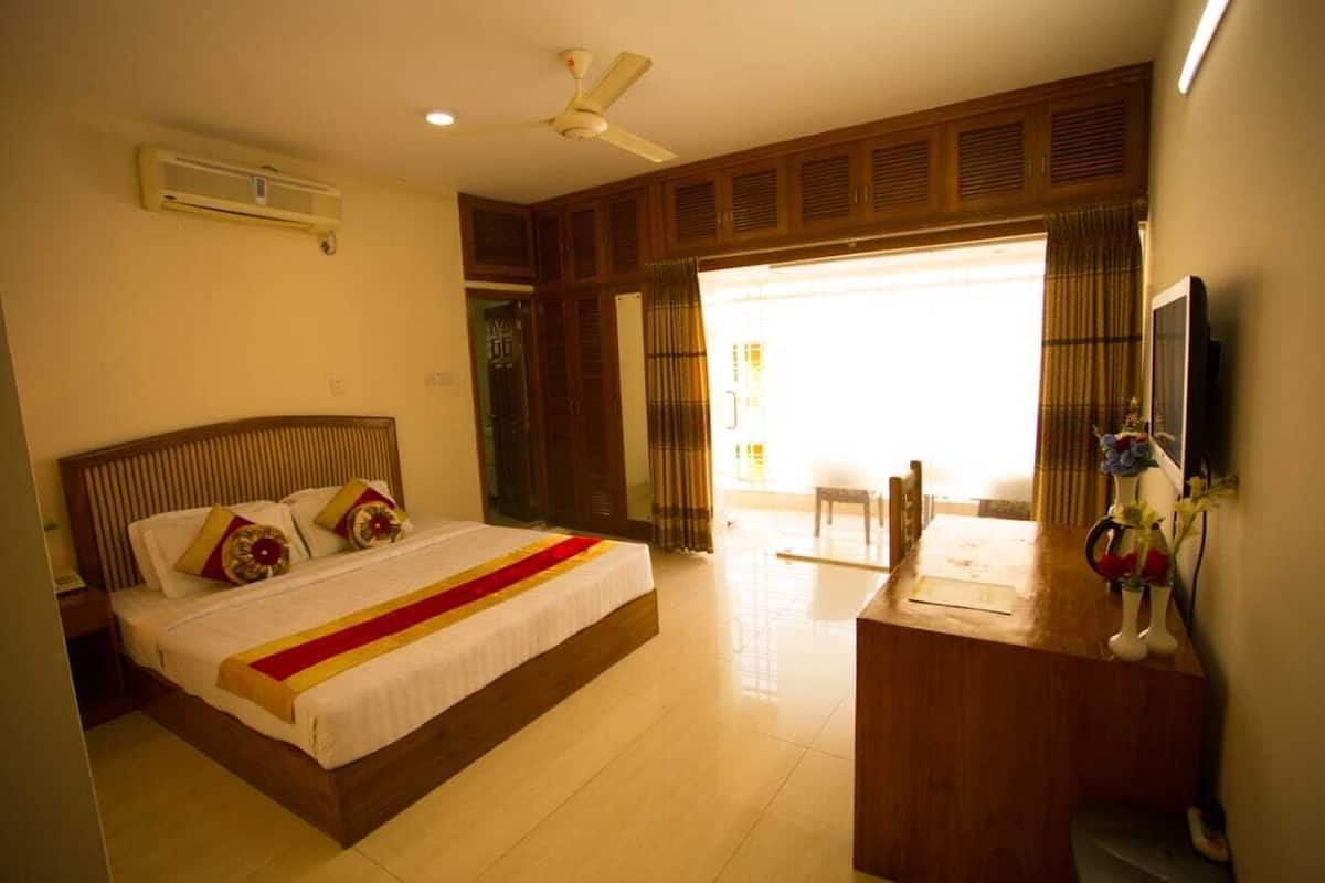 A hotel room with a bed, a desk, a chair, a TV, and an air conditioning unit.