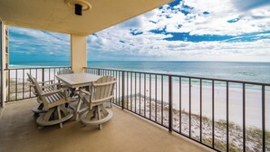 Een balkon met een tafel en stoelen met uitzicht op een strand en een heldere lucht.