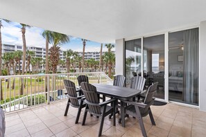 A balcony with a table and chairs, overlooking a pool and palm trees.