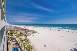 Blick auf einen Strand von einem Balkon mit Pool, Palmen und blauem Himmel.