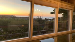 A modern interior with large windows offering a view of a sunset over a coastal landscape.