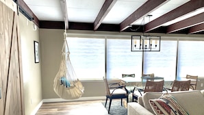 A spacious living room with a hanging macrame chair, a sofa with a patterned throw, and a view of the ocean through large windows.