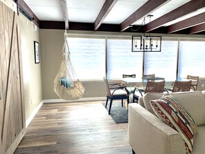 A spacious living room with a hanging macrame chair, a sofa with a patterned throw, and a view of the ocean through large windows.