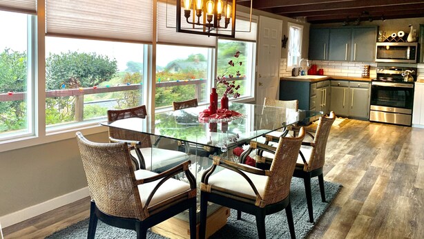 A modern kitchen with a glass dining table, wicker chairs, and a hanging light fixture.