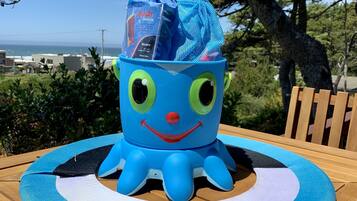 A blue inflatable pool float with a smiling face and the word "BEAMO" on a wooden deck with a view of the ocean and trees in the background.