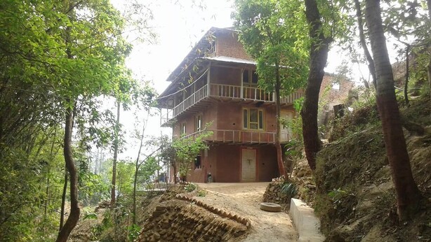 A rustic two-story house with a balcony, surrounded by dense forest. - Nagarkot Community Homestay (Mahamanjushree Nagarkot)