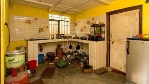 A kitchen with yellow walls, white cabinets, and a white refrigerator. There are various kitchen utensils and cookware on the countertops and hanging from the ceiling. - Nagarkot Community Homestay (Mahamanjushree Nagarkot)