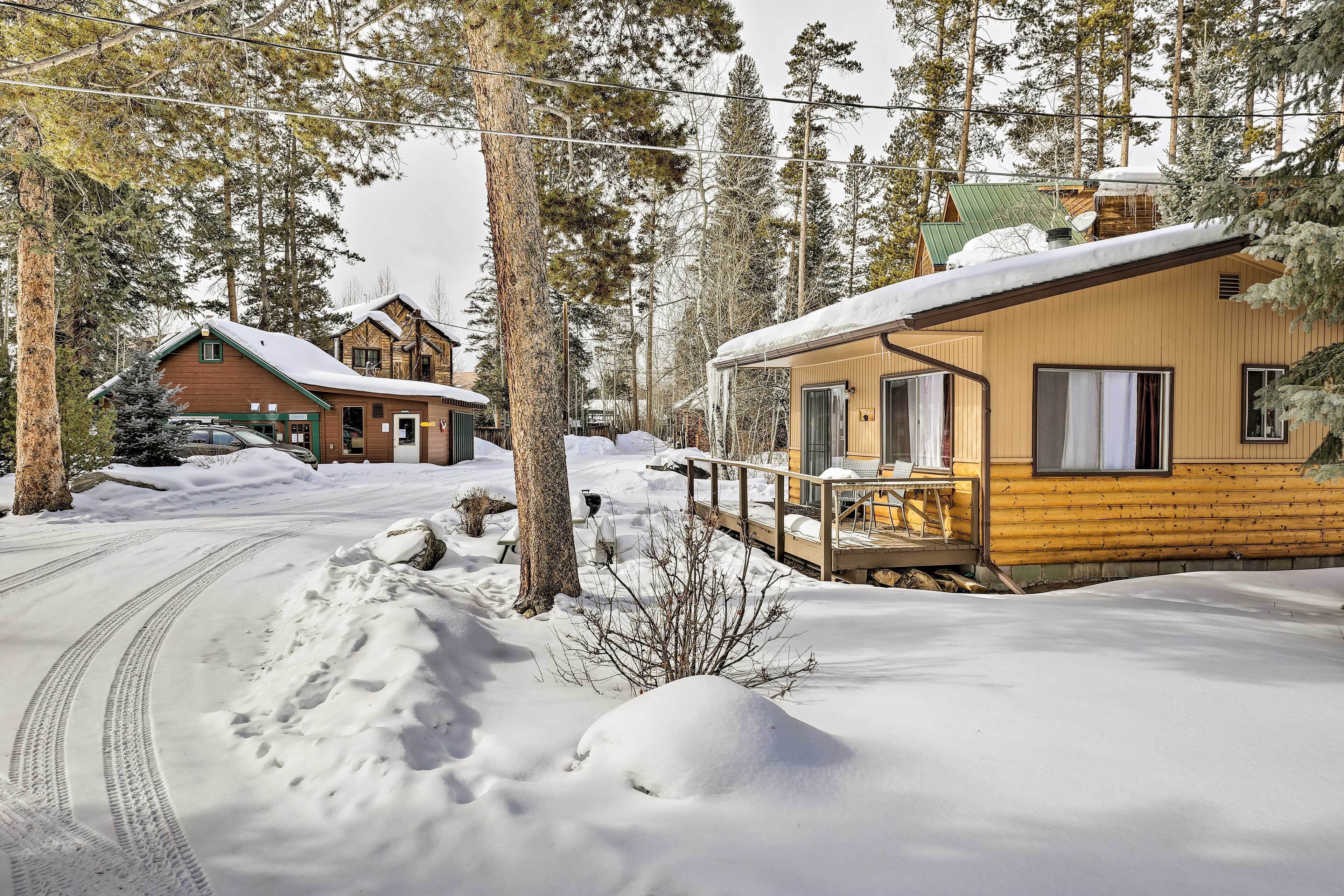 A cabin with a wooden exterior, a porch, and a snow-covered driveway.