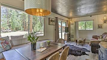 A spacious room with a large wooden dining table, a comfortable seating area, and a view of the forest through large windows.