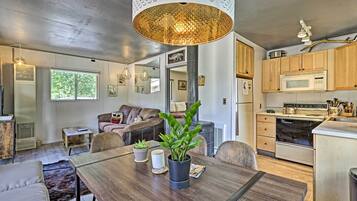 A modern kitchen with wooden cabinets, a microwave, and a stove. There is a dining area with a wooden table and chairs, and a large potted plant.