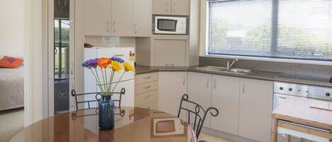 A compact kitchen with a microwave, stove, and sink. There's a dining table with a vase of flowers.