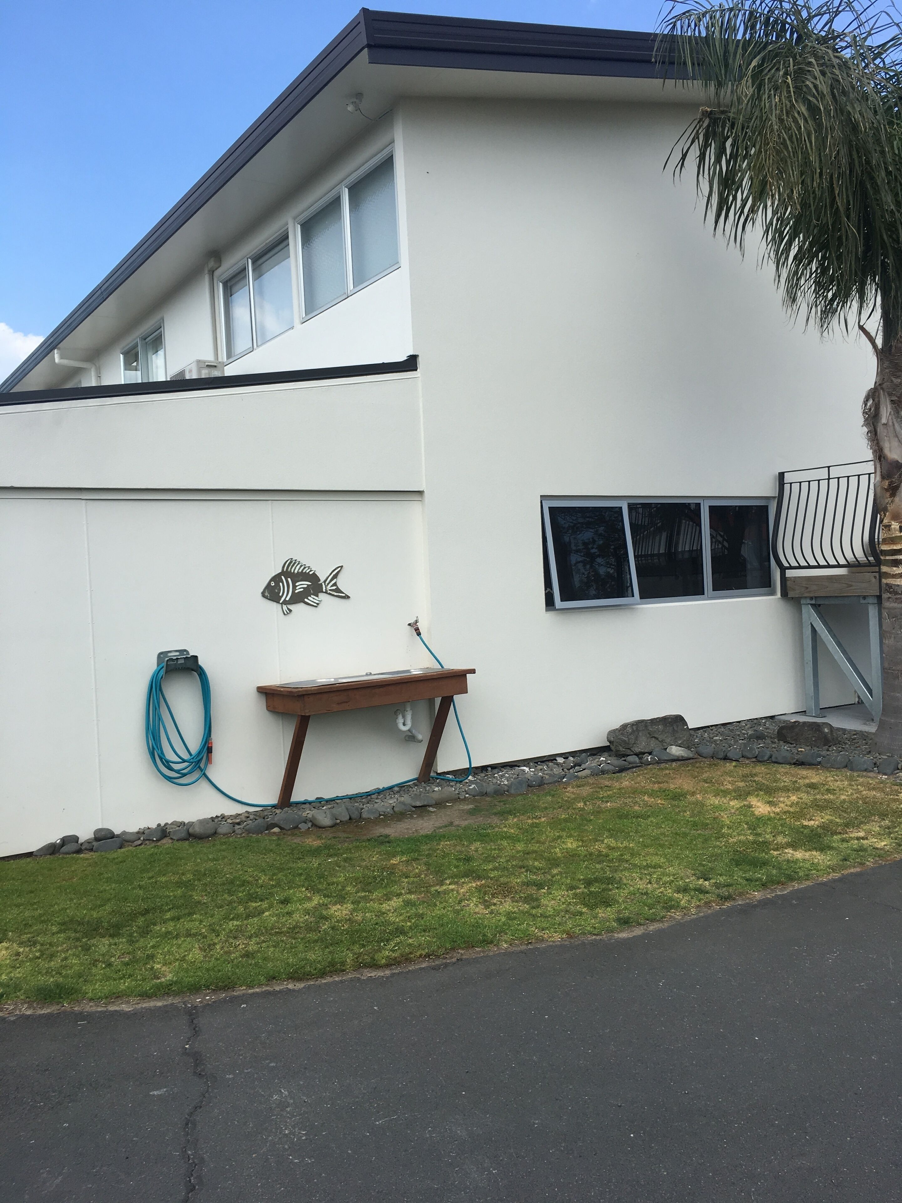 A white building with a small deck, a hose, and a bench.