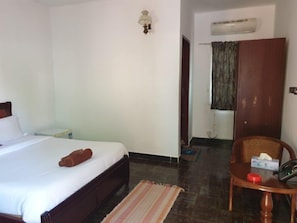 Habitación de hotel con cama, una silla, una mesita de noche, aire acondicionado instalado en la pared y una puerta con cortina.