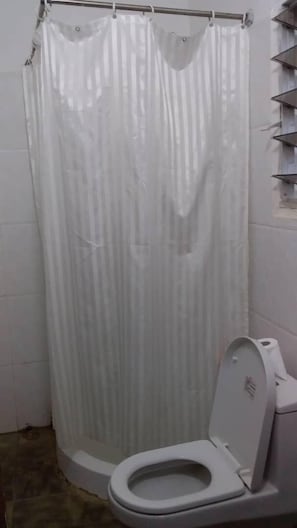 Un baño con inodoro, cortina de ducha y pared de azulejos.
