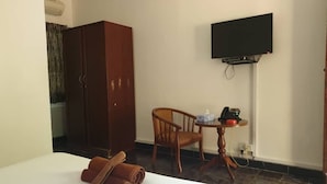 Ein Hotelzimmer mit einem Bett, einem Holzschrank, einem an der Wand befestigten Fernseher, einem kleinen Holztisch mit Stuhl und einem zusammengerollten Handtuch auf dem Bett.