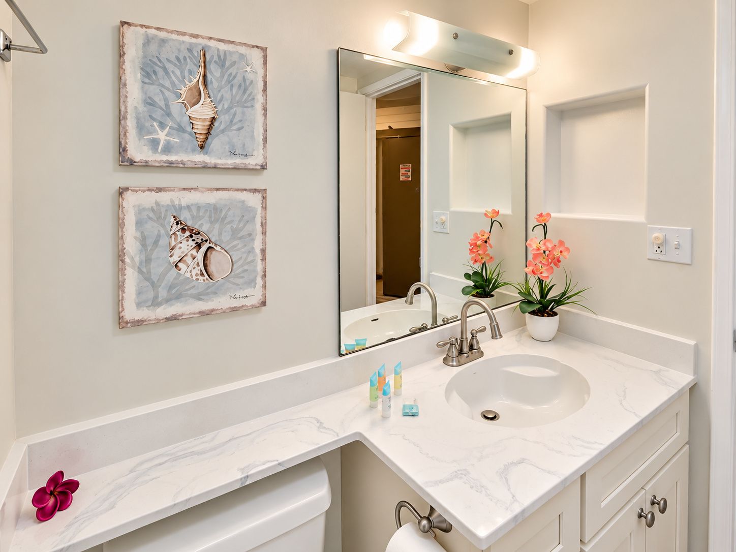 A bathroom with a marble sink, a large mirror, and two framed artworks on the wall.