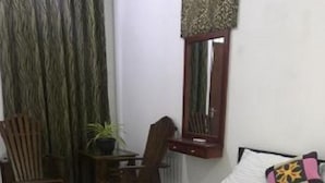 A neatly made bed with a rolled towel, a wooden chair, a desk with a mirror, and a potted plant. - Atozee Airport villa (Seeduwa - Katunayake)