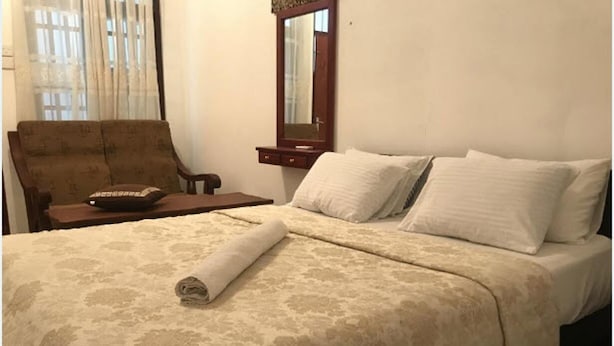 A hotel room with a bed, a chair, a nightstand, and a mirror. - Atozee Airport villa (Seeduwa - Katunayake)