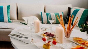 Un coin repas avec une table blanche dressée pour deux personnes, agrémentée d’une bougie, de verres et d’une assiette de nourriture.