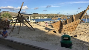 Una spiaggia con barche di legno, un'area giochi con reti e un cestino verde.