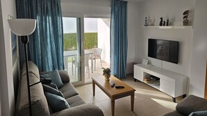 Un soggiorno moderno con divano, tavolino, televisione e un balcone con tende.